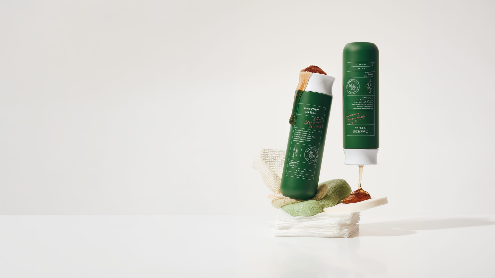 Dos frascos verdes de tónico de una marca coreana sobre una pila de discos de algodón